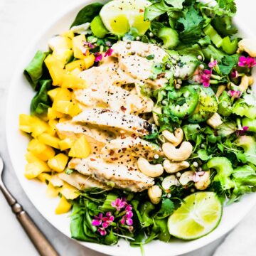 A white bowl filled with curried chicken salad served over mixed greens with spicy mango chutney.