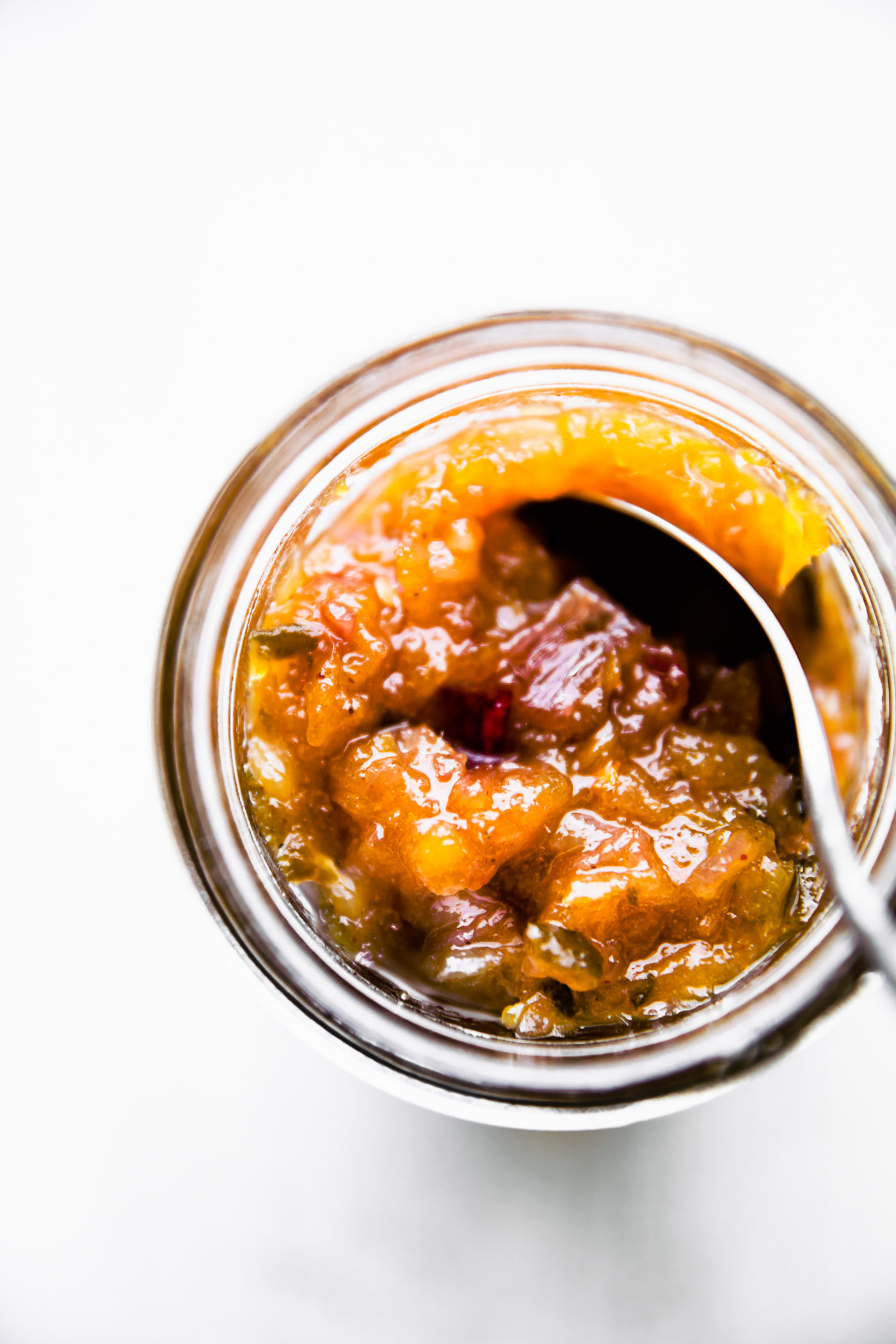 Jalapeño mango chutney in mason jar being stirred with spoon.