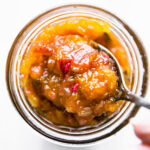 A spoonful of jalapeño mango chutney hovering above mason jar filled with chutney