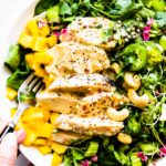 Two hands holding bowl filled with curried chicken salad with spicy mango chutney.