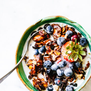 Grain free granola clusters in turquoise bowl with yogurt and fresh berries.