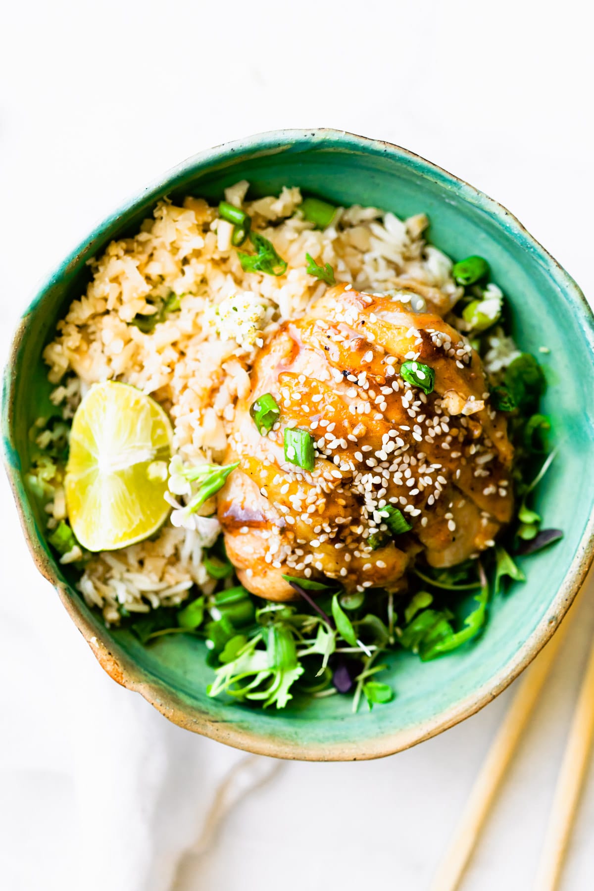 Overhead view teriyaki chicken thigh served over rice in turquoise bowl.