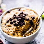 Vanilla mug cake in white mug topped with chocolate chips with spoon in cake