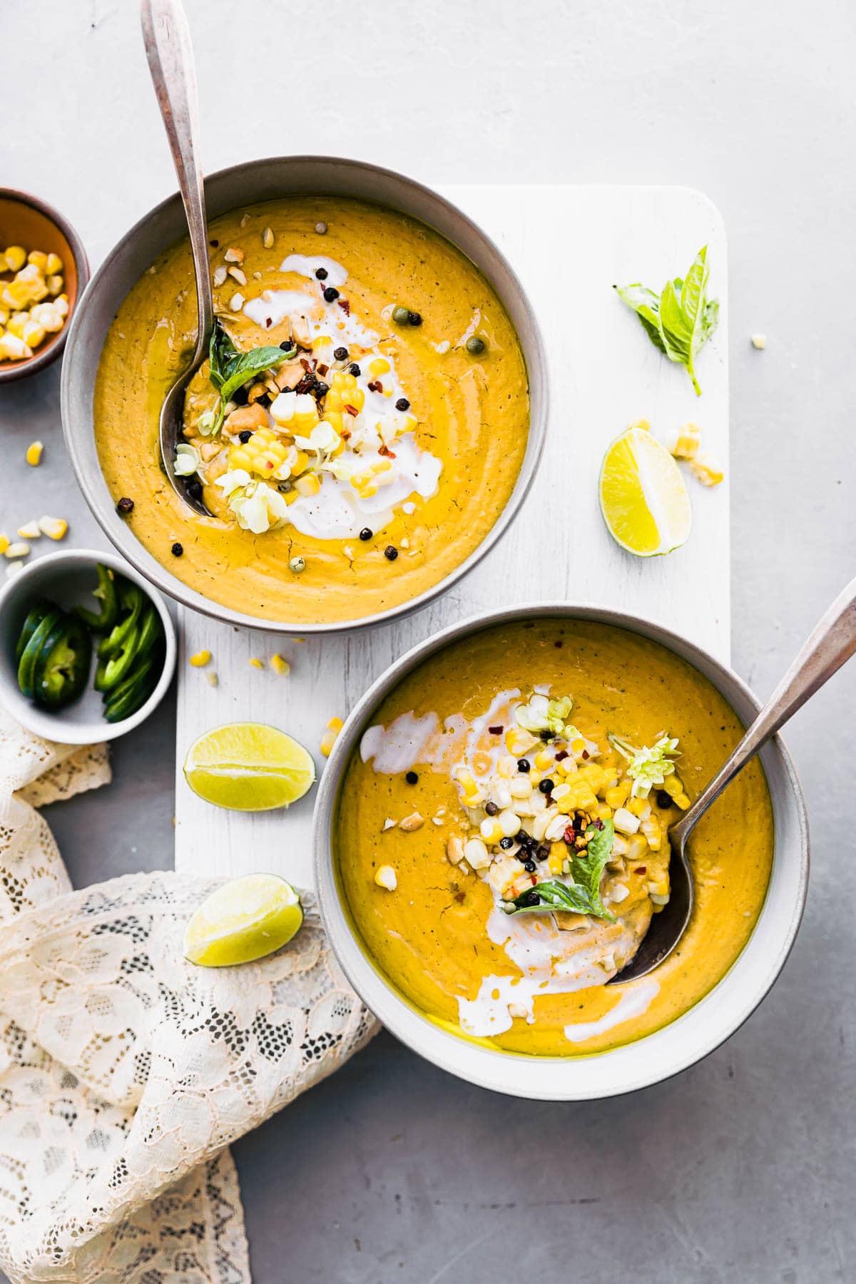 two bowls of vegan corn soup with spoons in them