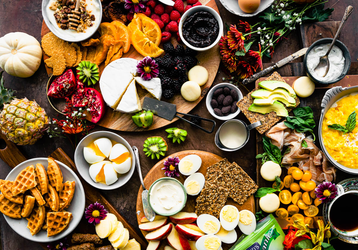 Overhead view brunch charcuterie boards with flower arrangements scattered between.