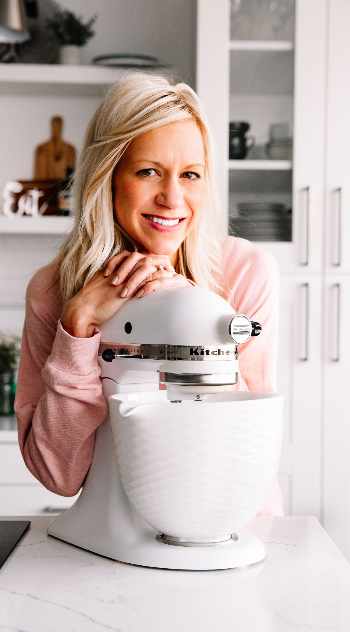 Woman wearing pink shirt with kitchenaid mixer in front of her on countertop.