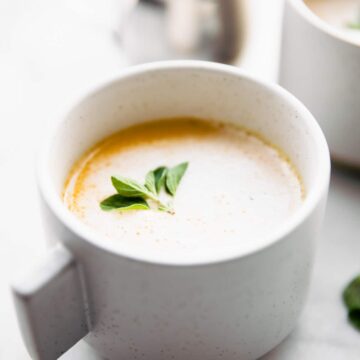Bone broth latte in a white mug topped with a sprig of green herbs.