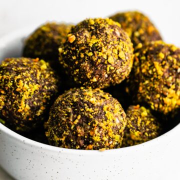 chocolate pistachio balls stacked in a white bowl.