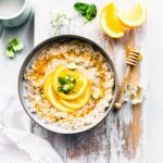Orange vanilla protein overnight oats served in bowl topped with fresh orange slices sitting on white cutting board.