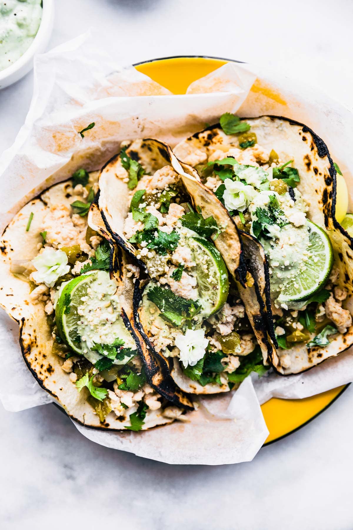 Three char burned corn tortillas filled with green chile turkey taco fillings plated on round yellow tray.