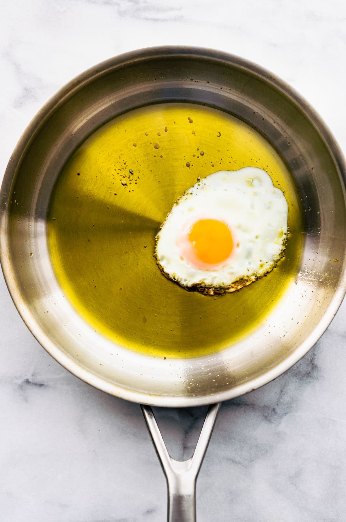 A fried egg in a skillet with a thick coating of olive oil.
