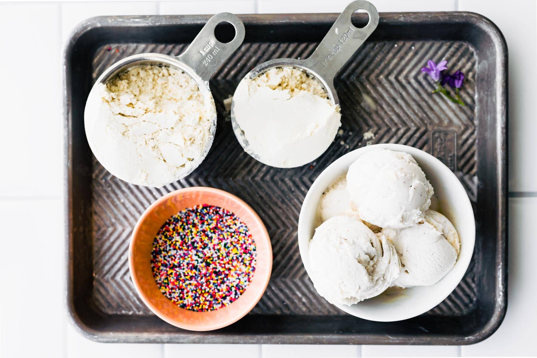 Scoops of vanilla ice cream, colorful sprinkles, and gluten free flour on a baking sheet.