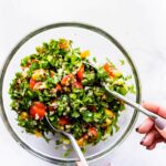 tossing gluten free tabbouleh salad ingredients in large glass bowl