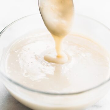 powdered sugar coconut milk mixture dripping from spoon into a glass bowl beneath it