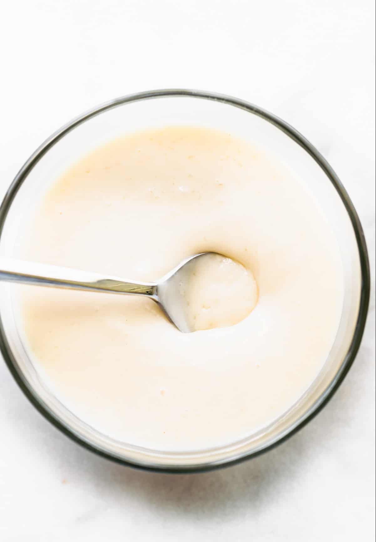 glass bowl of homemade sweetened condensed milk with spoon in it