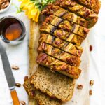 overhead photo: loaf of low carb banana bread cut into slices on wooden board next to knife and honey