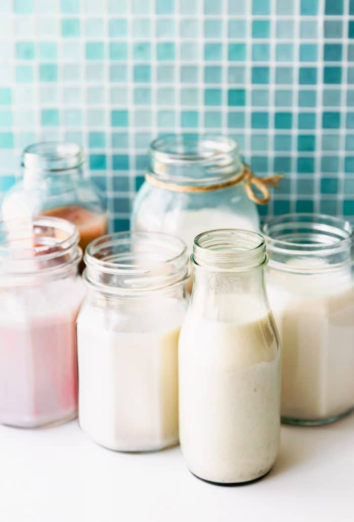 dairy free strawberry milk and nut milk in small glass jars and bottles on white countertop