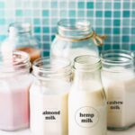 small glass bottles and mason jars filled with cashew milk, hemp milk, and almond milk