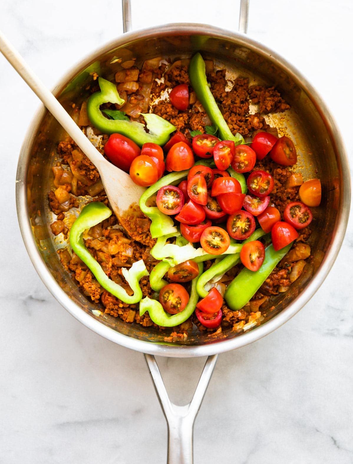 overhead photo: sliced cherry tomatoes and green bell pepper slices in skillet with crumbled chorizo