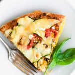close up overhead photo: slice of crustless zucchini pie on white plate with fork