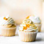 2 vegan cupcakes in paper liners topped with swirl of vegan cream cheese frosting