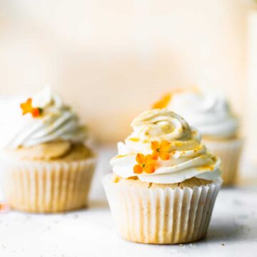 2 vegan cupcakes in paper liners topped with swirl of vegan cream cheese frosting