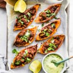 overhead photo: hands holding parchment paper lined tray of sweet potato skins filled with chili