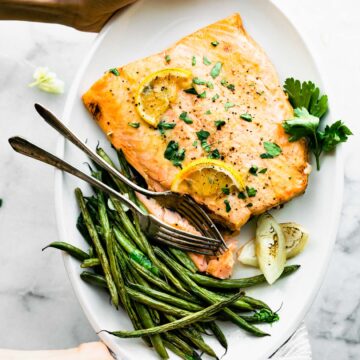 overhead: woman's hands holding plate of maple mustard salmon with French green beans