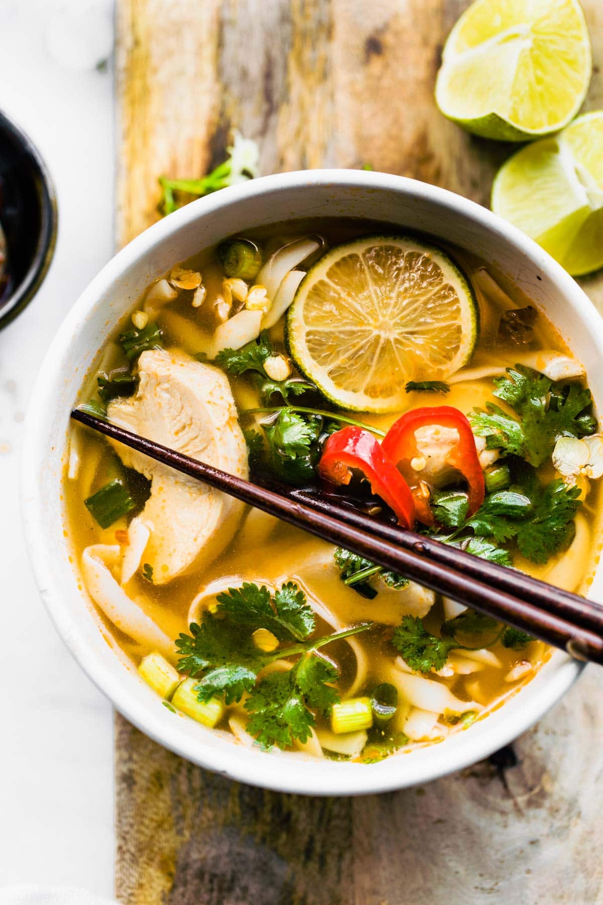 Overhead photo of chopsticks in a white bowl of Thai Chicken Soup on wooden board.