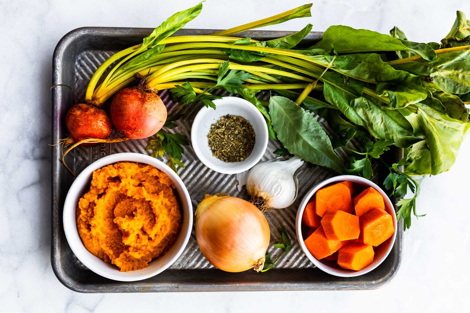 Fresh ingredients on a baking sheet to make a nightshade free nomato sauce.