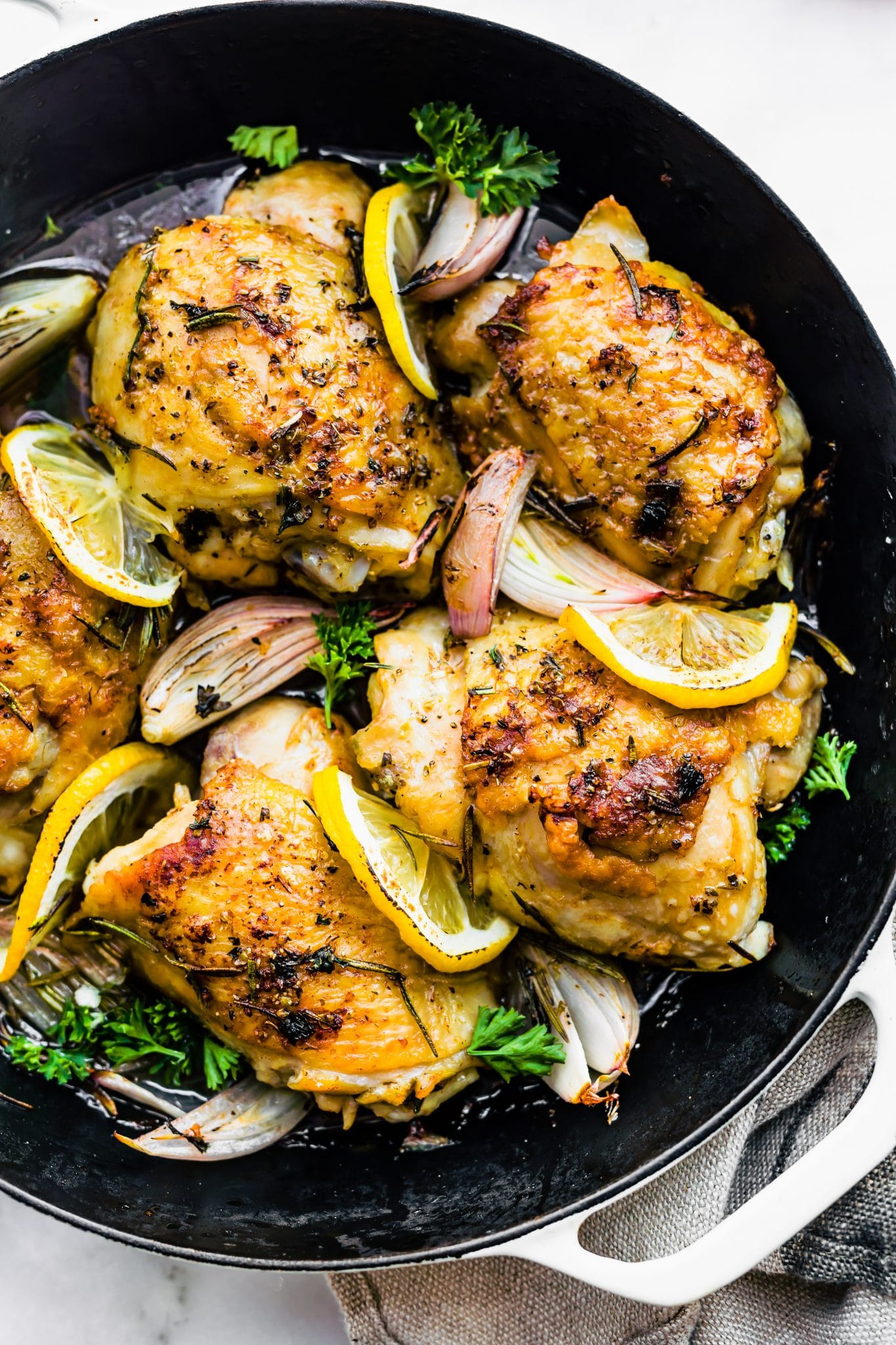 overhead image: herb roasted chicken thighs in skillet with lemon slices and fresh herbs