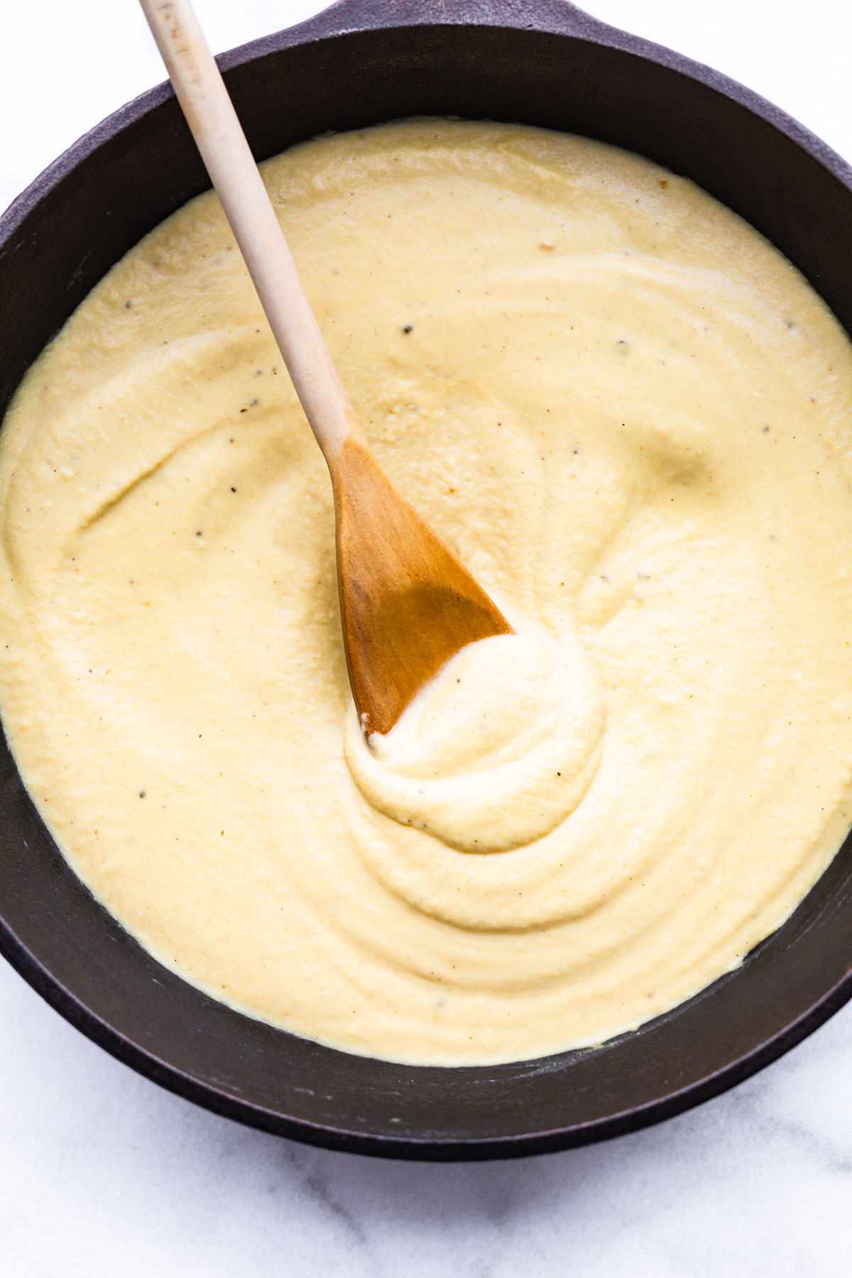 wooden spoon in pan of dairy free alfredo sauce