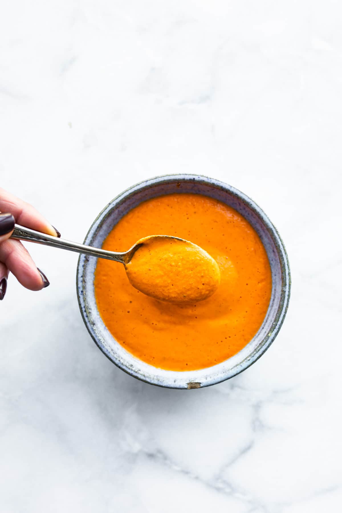 overhead: spoonful of roasted red pepper sauce over bowl of sauce