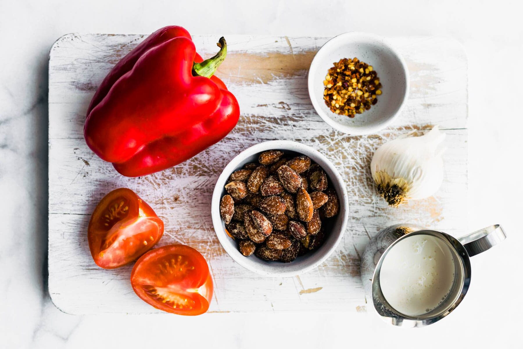 ingredients to make roasted red pepper sauce on white wooden cutting board