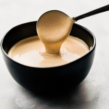 A spoon dripping homemade yum yum sauce back into a small bowl.