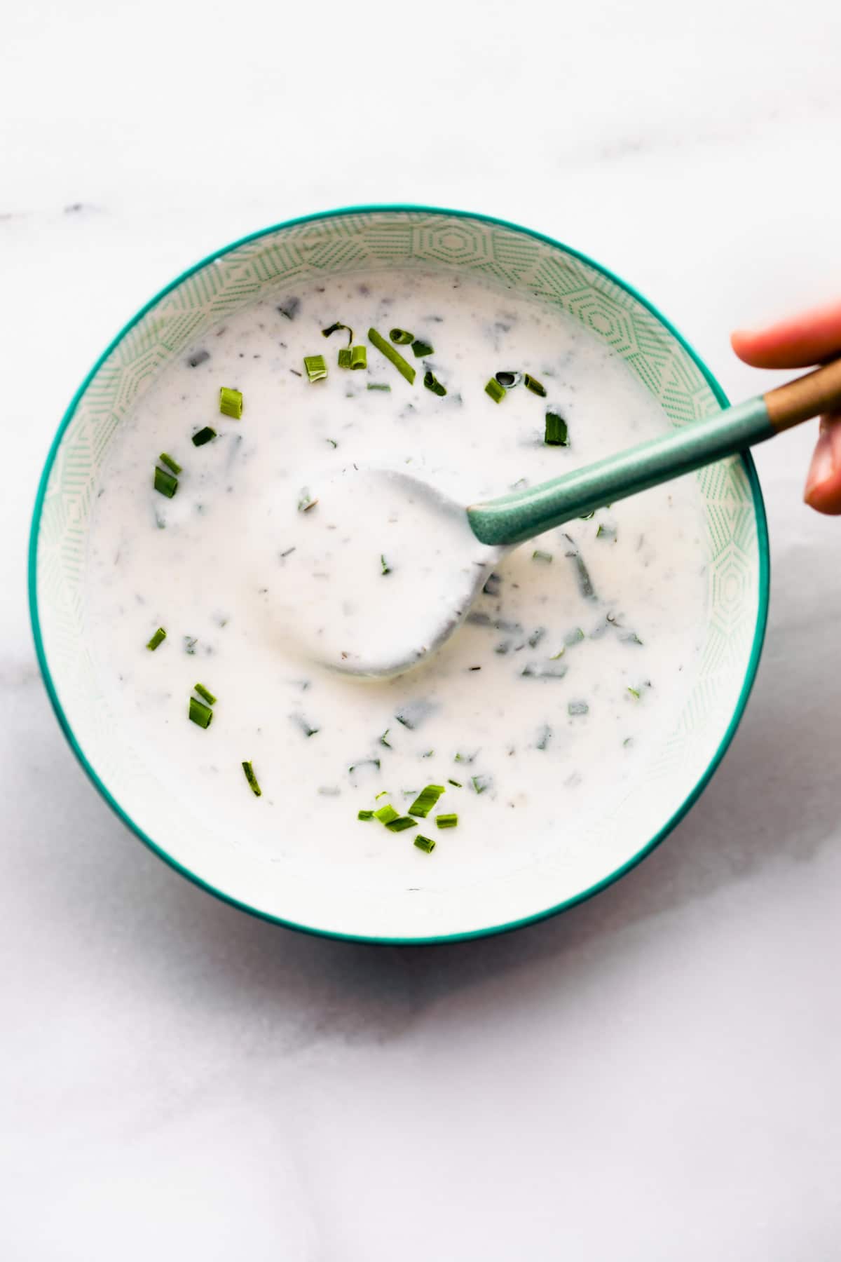 spicy vegan ranch in patterned turquoise bowl with spoon in ranch dressing.