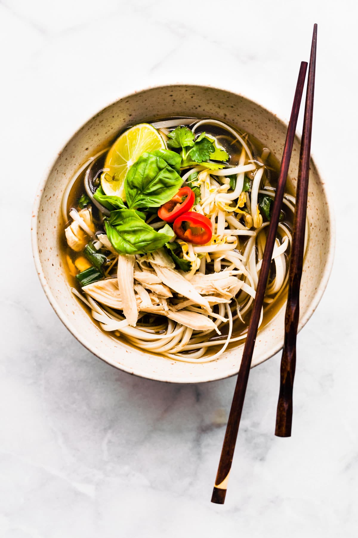 Overhead photo of chopsticks on a bowl of chicken pho ga with rice noodles.