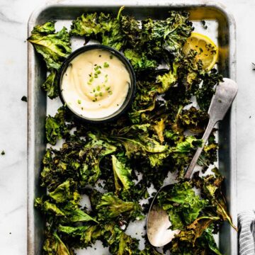 Overhead image of prepared crispy kale chips with vegan ranch dipping sauce cup on a cookie sheet