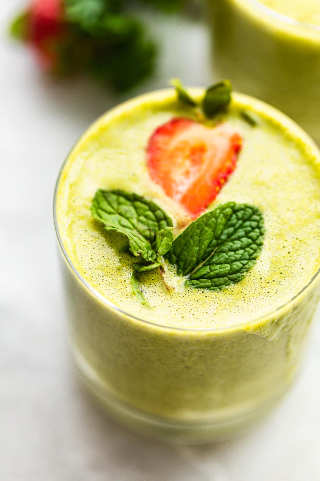 Image of a glass filled with blended super fruit kale smoothie, topped with fresh mint and strawberry