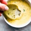 An artichoke leaf being dipped into a bowl of garlic aioli.