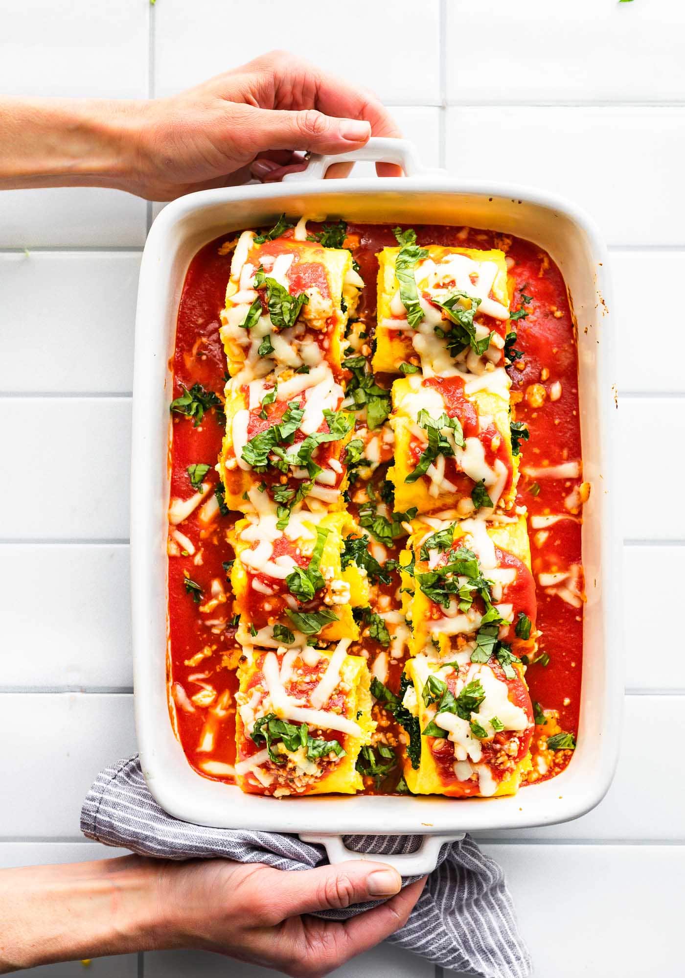 Overhead image of prepared keto egg lasagna roll ups in casserole dish covered in tomato sauce, cheese, and herbs