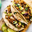 Overhead image of vegan taco meat in tortillas with avocado on a wooden platter.