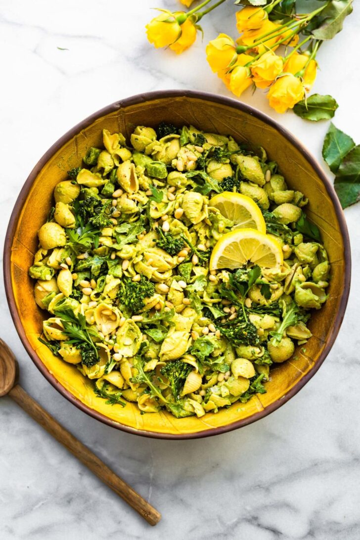 Green goddess pasta salad on a tabletop with yellow flowers and a wooden spoon.