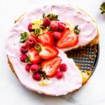 Overhead image of flourless almond cake dressed with yogurt frosting, fresh berries, and edible flowers.