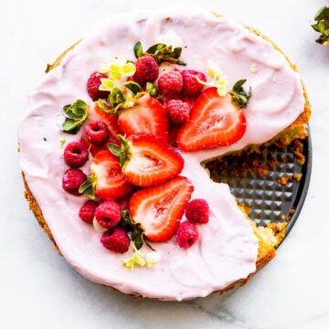 Overhead image of flourless almond cake dressed with yogurt frosting, fresh berries, and edible flowers.