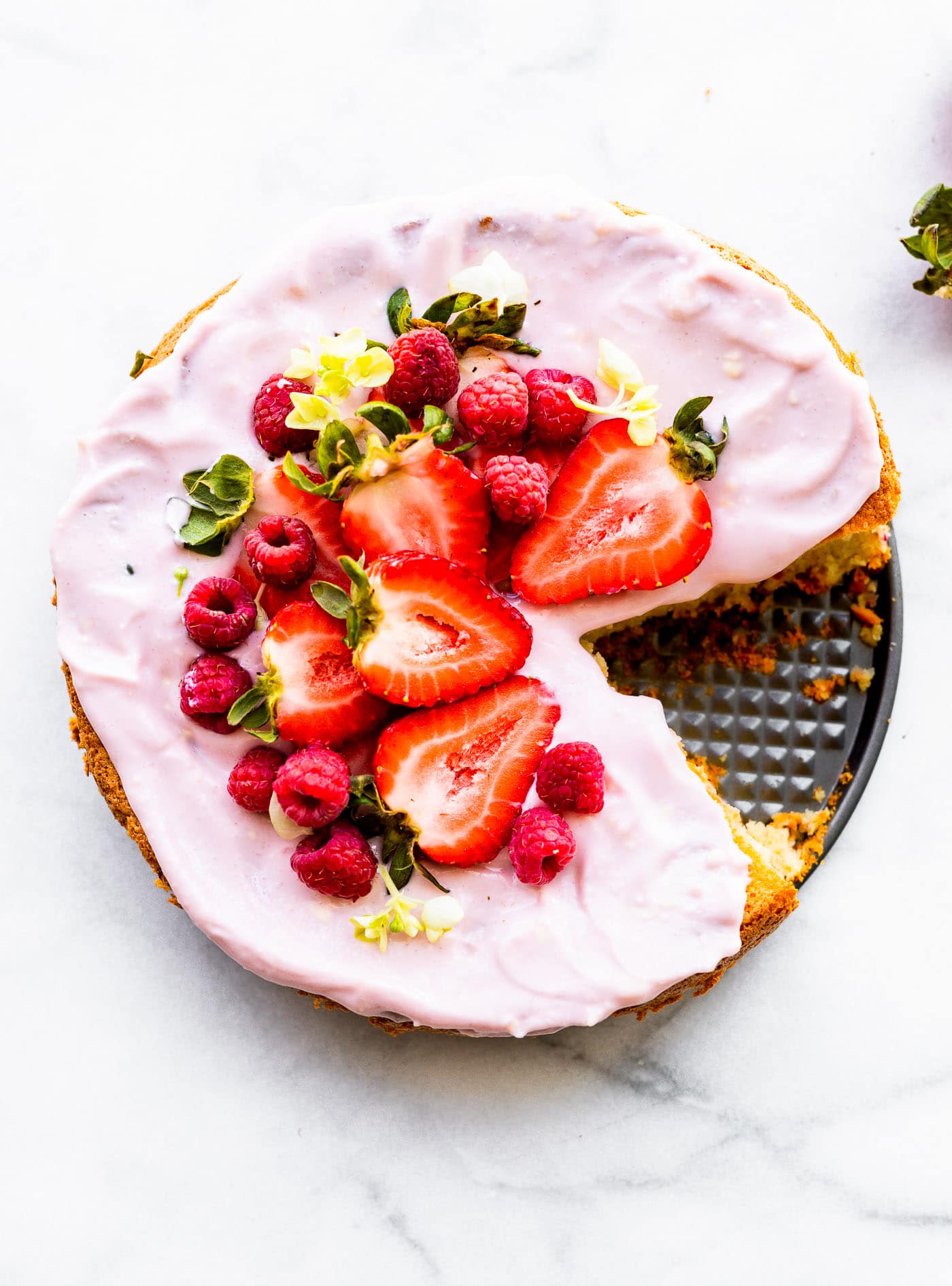 Overhead image of flourless almond cake dressed with yogurt frosting, fresh berries, and edible flowers.