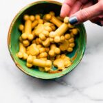 Homemade frozen dog treats in the shape of bones and paw prints being pulled out of a small green bowl