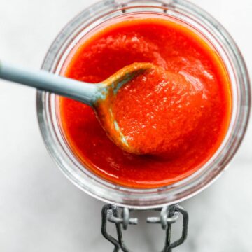 Overhead image of a spoonful of homemade sriracha sauce being lifted out of a storage jar.