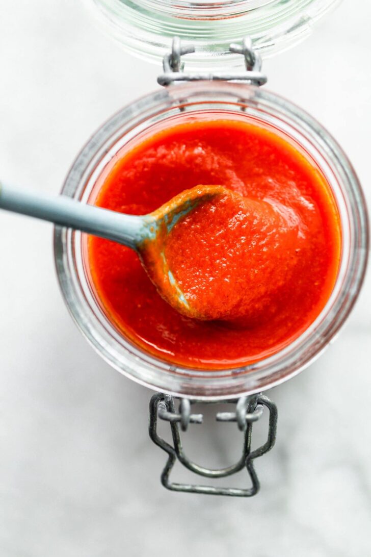 Overhead image of a spoonful of homemade sriracha sauce being lifted out of a storage jar.