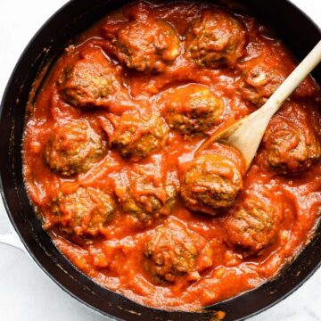 Overhead image of a skillet with meatballs and sauce with a wooden spoon.